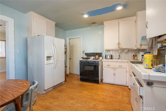 kitchen featuring tile counters, range with gas stovetop, white cabinets, white refrigerator with ice dispenser, and backsplash