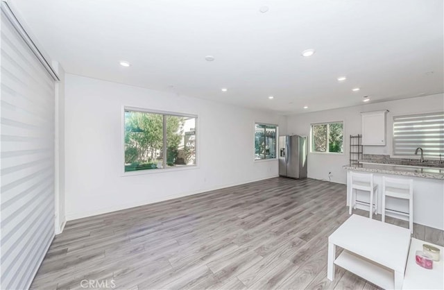 kitchen with sink, light hardwood / wood-style flooring, stainless steel fridge, light stone countertops, and white cabinets