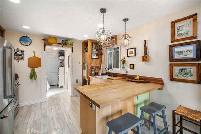 kitchen featuring butcher block countertops, stainless steel fridge, a kitchen bar, decorative light fixtures, and kitchen peninsula