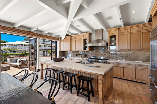 kitchen featuring a kitchen island with sink, wall chimney range hood, range, and decorative backsplash