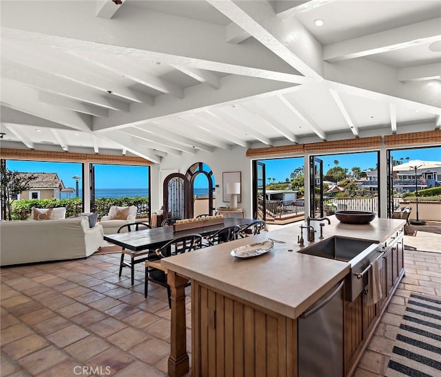 kitchen with an island with sink, sink, stainless steel dishwasher, and vaulted ceiling with beams