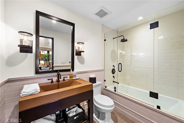 full bathroom featuring enclosed tub / shower combo, toilet, sink, and tile walls