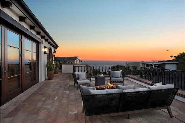 patio terrace at dusk featuring a water view and an outdoor living space with a fire pit