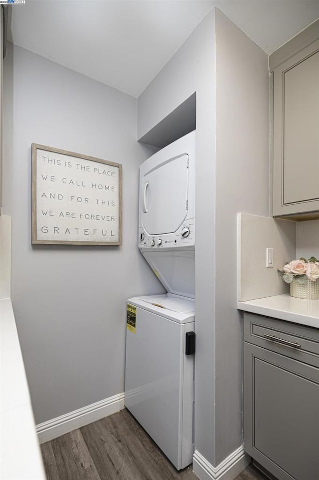 clothes washing area with cabinets, stacked washer / dryer, and dark hardwood / wood-style flooring