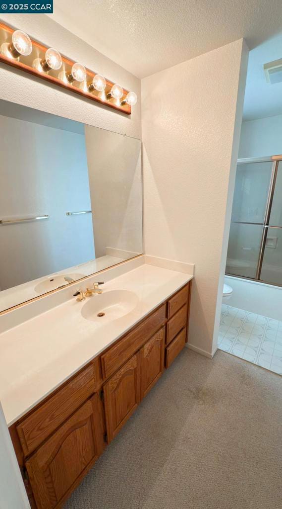 full bathroom with vanity, a textured ceiling, shower / bath combination with glass door, and toilet