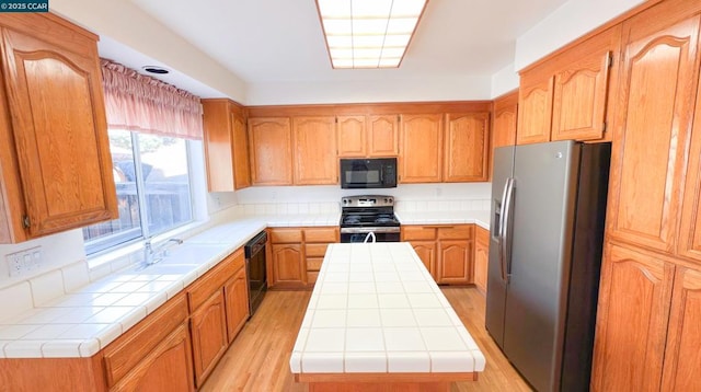 kitchen with a kitchen island, sink, tile counters, black appliances, and light hardwood / wood-style flooring