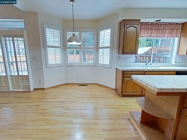 kitchen with light hardwood / wood-style flooring, hanging light fixtures, tile countertops, and sink