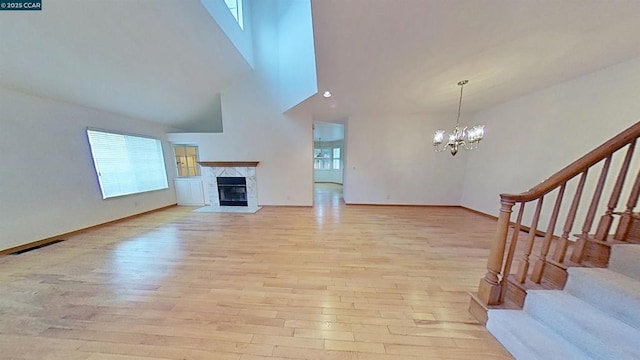 unfurnished living room with a notable chandelier, a towering ceiling, a high end fireplace, and light wood-type flooring