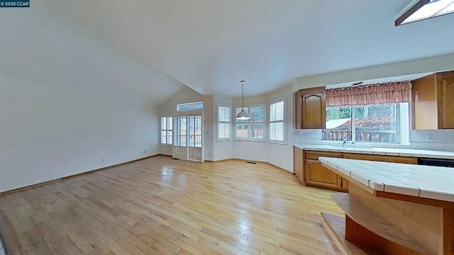 kitchen with pendant lighting, tile countertops, dishwasher, lofted ceiling, and light wood-type flooring