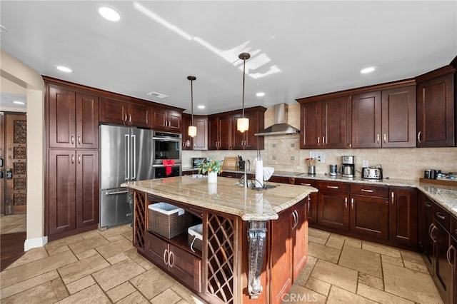 kitchen with decorative light fixtures, a center island, appliances with stainless steel finishes, light stone countertops, and wall chimney range hood