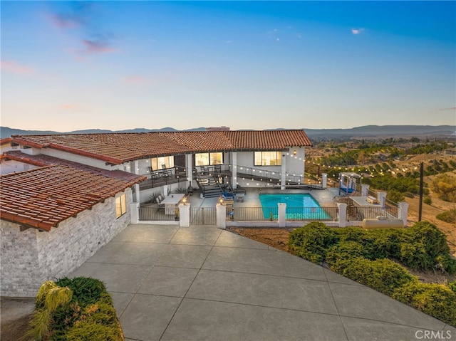 pool at dusk featuring a mountain view, fence, a gate, a fenced in pool, and a patio area