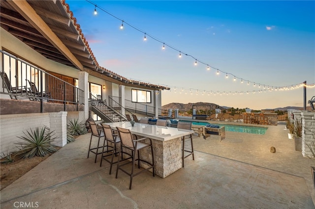 patio terrace at dusk with a fenced in pool and an outdoor bar