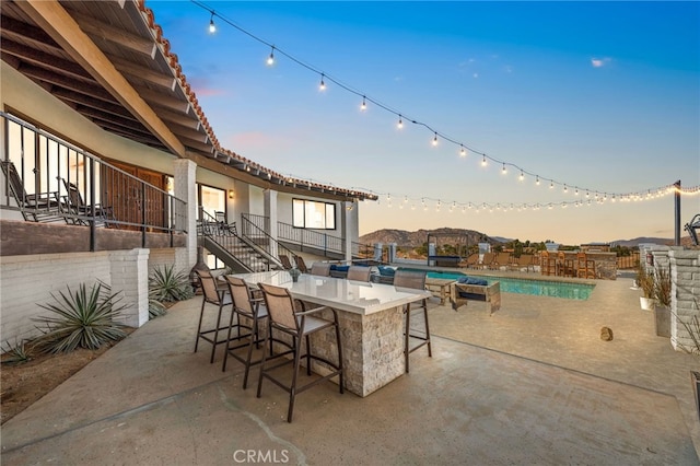 patio terrace at dusk featuring an outdoor pool, stairs, and outdoor dry bar