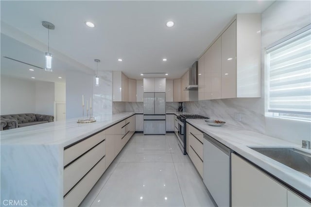 kitchen featuring backsplash, pendant lighting, stainless steel appliances, light stone countertops, and wall chimney range hood