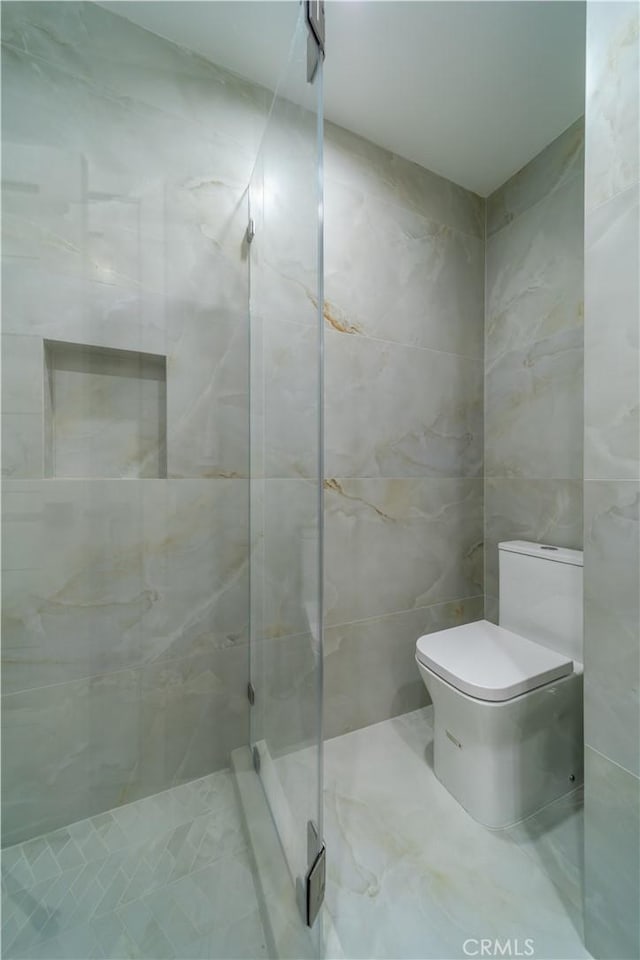 bathroom featuring an enclosed shower, tile walls, and toilet