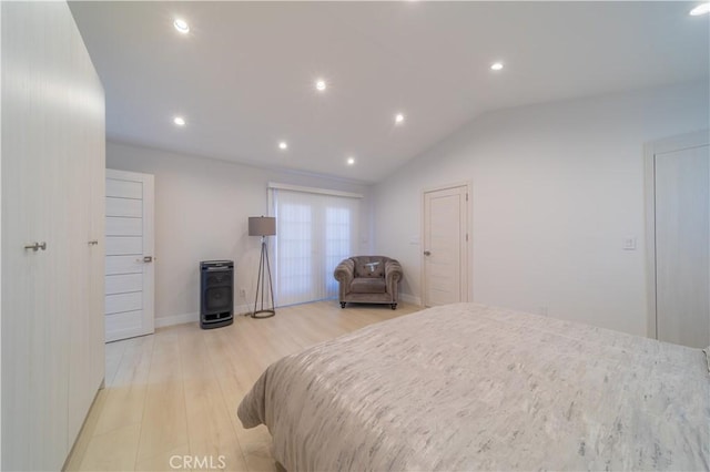 bedroom with vaulted ceiling, a wood stove, and light hardwood / wood-style flooring