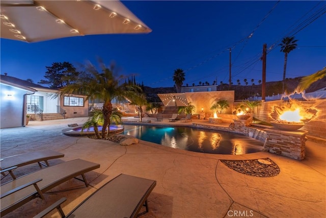 pool at night with a patio and a fire pit