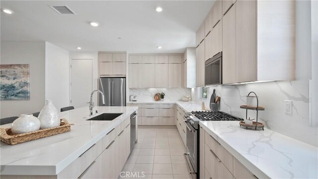 kitchen with sink, light tile patterned floors, appliances with stainless steel finishes, backsplash, and light stone counters