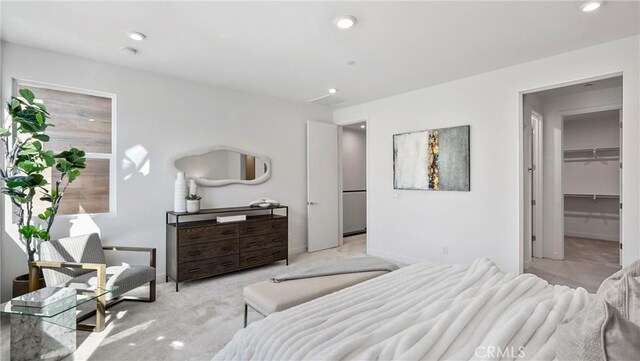 bedroom featuring a walk in closet, light carpet, and a closet