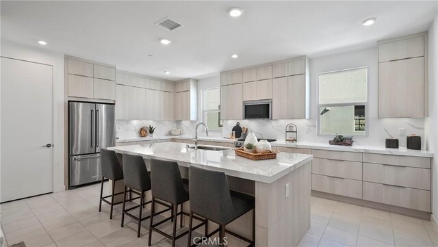 kitchen featuring light tile patterned flooring, a breakfast bar area, stainless steel appliances, and a center island with sink