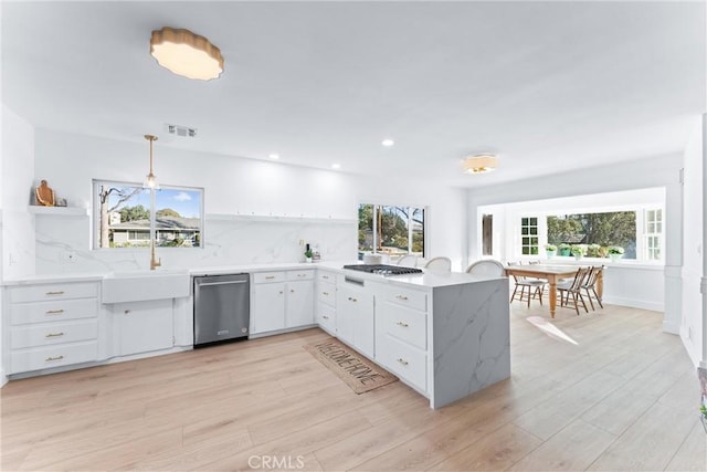 kitchen with appliances with stainless steel finishes, hanging light fixtures, tasteful backsplash, white cabinets, and kitchen peninsula