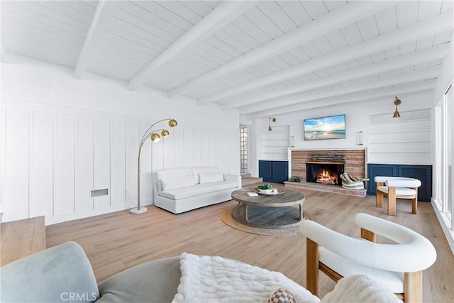 living room featuring beam ceiling, a fireplace, and light wood-type flooring