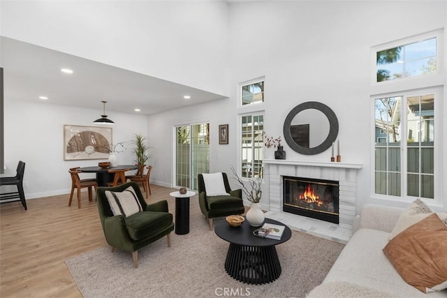 living room with a high ceiling, a healthy amount of sunlight, a fireplace, and light hardwood / wood-style floors