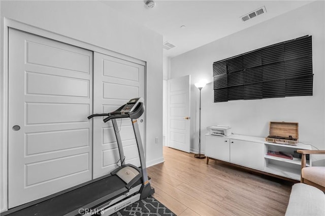 workout area featuring light wood finished floors, visible vents, and baseboards