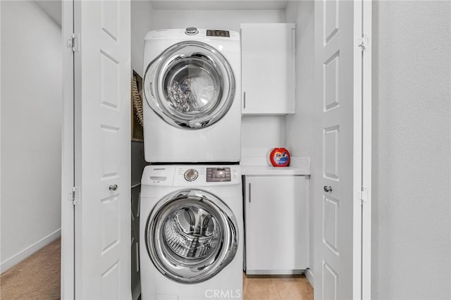 washroom featuring light colored carpet, baseboards, cabinet space, and stacked washing maching and dryer