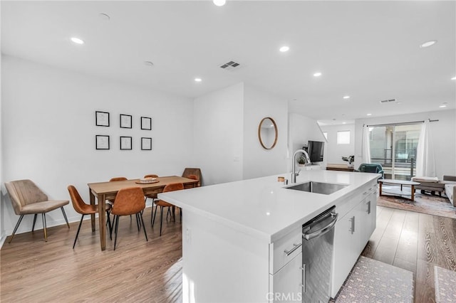 kitchen featuring light wood-style flooring, a sink, white cabinets, dishwasher, and an island with sink