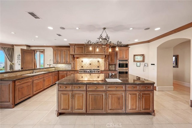 kitchen with tasteful backsplash, hanging light fixtures, sink, and dark stone countertops