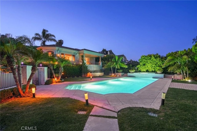 pool at dusk with a patio area and a lawn