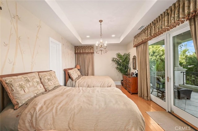 bedroom with light hardwood / wood-style flooring, access to exterior, an inviting chandelier, and a tray ceiling