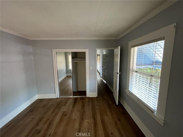 unfurnished bedroom with multiple windows, ornamental molding, dark hardwood / wood-style floors, and a closet