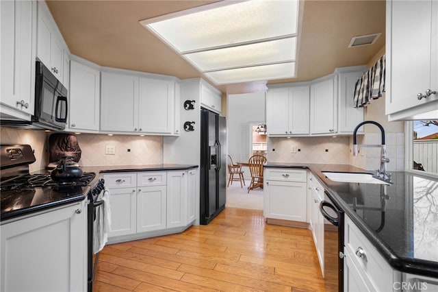 kitchen featuring a wealth of natural light, white cabinetry, sink, black appliances, and light wood-type flooring