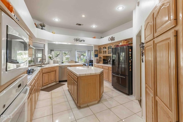 kitchen featuring sink, light tile patterned floors, appliances with stainless steel finishes, a center island, and tile countertops