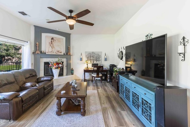 living room with ceiling fan, a tiled fireplace, and hardwood / wood-style floors