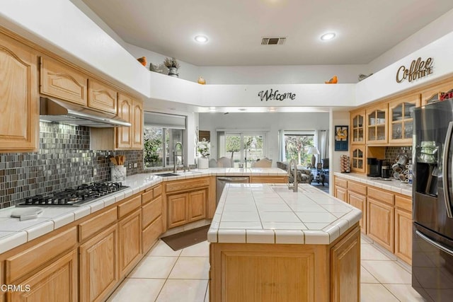 kitchen with appliances with stainless steel finishes, tile countertops, sink, backsplash, and a center island