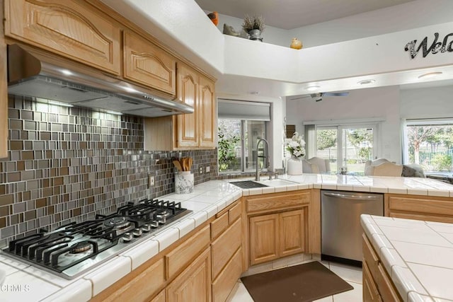 kitchen with appliances with stainless steel finishes, sink, decorative backsplash, tile counters, and wall chimney exhaust hood