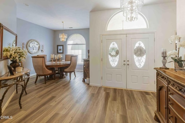 entrance foyer with french doors, a notable chandelier, and light hardwood / wood-style flooring