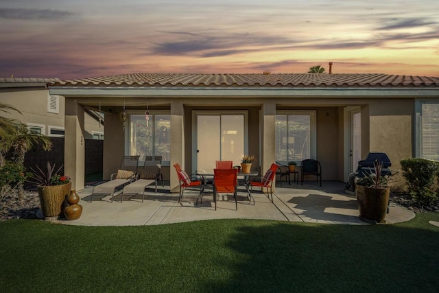 back house at dusk featuring a yard and a patio area