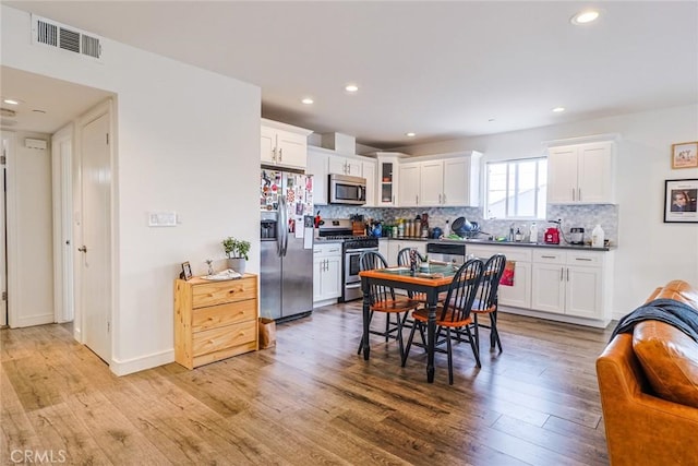 kitchen featuring backsplash, stainless steel appliances, light wood-type flooring, and white cabinets