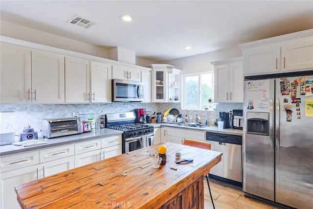 kitchen with stainless steel appliances, butcher block counters, white cabinets, and backsplash