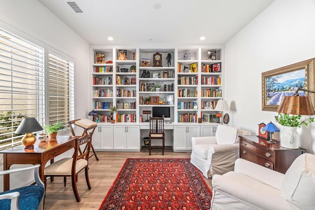 living area with built in shelves, built in desk, and light hardwood / wood-style flooring