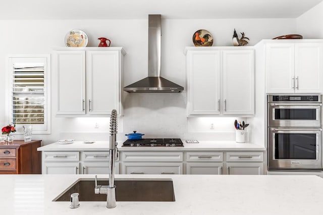 kitchen featuring white cabinetry, wall chimney range hood, sink, and appliances with stainless steel finishes