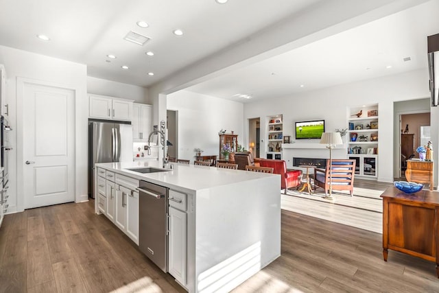 kitchen with built in shelves, sink, white cabinetry, a center island with sink, and stainless steel appliances