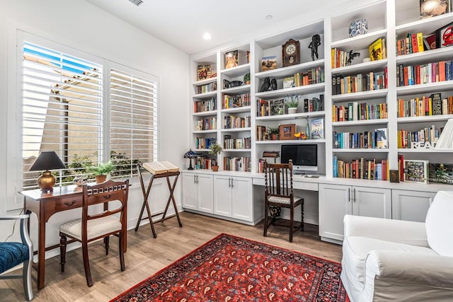 living area with built in shelves, built in desk, and light hardwood / wood-style floors