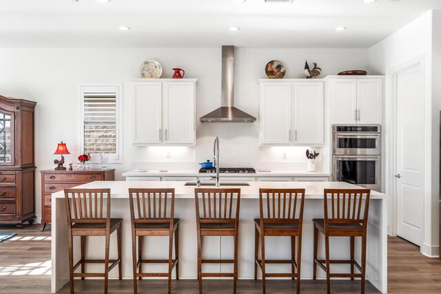 kitchen with white cabinetry, wall chimney range hood, a kitchen island with sink, and stainless steel appliances