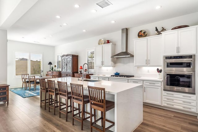 kitchen featuring a center island with sink, white cabinetry, sink, and wall chimney range hood