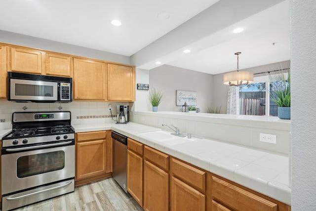 kitchen with sink, appliances with stainless steel finishes, backsplash, tile counters, and light hardwood / wood-style floors